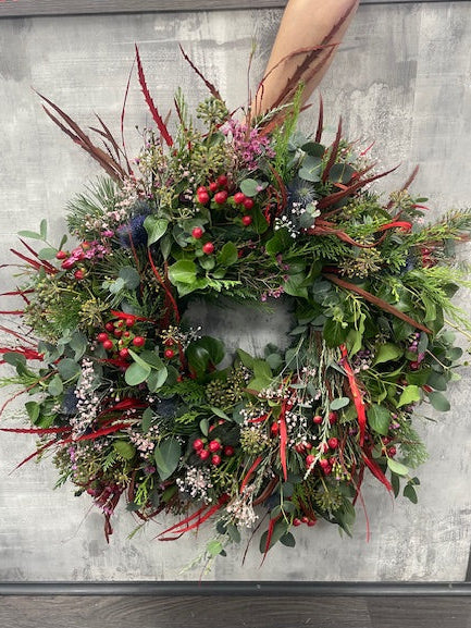 Decorative wreath with greenery and red accents on a noble fir base