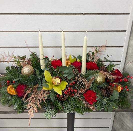 Decorative floral arrangement with candles and ornaments on a nobble fir base