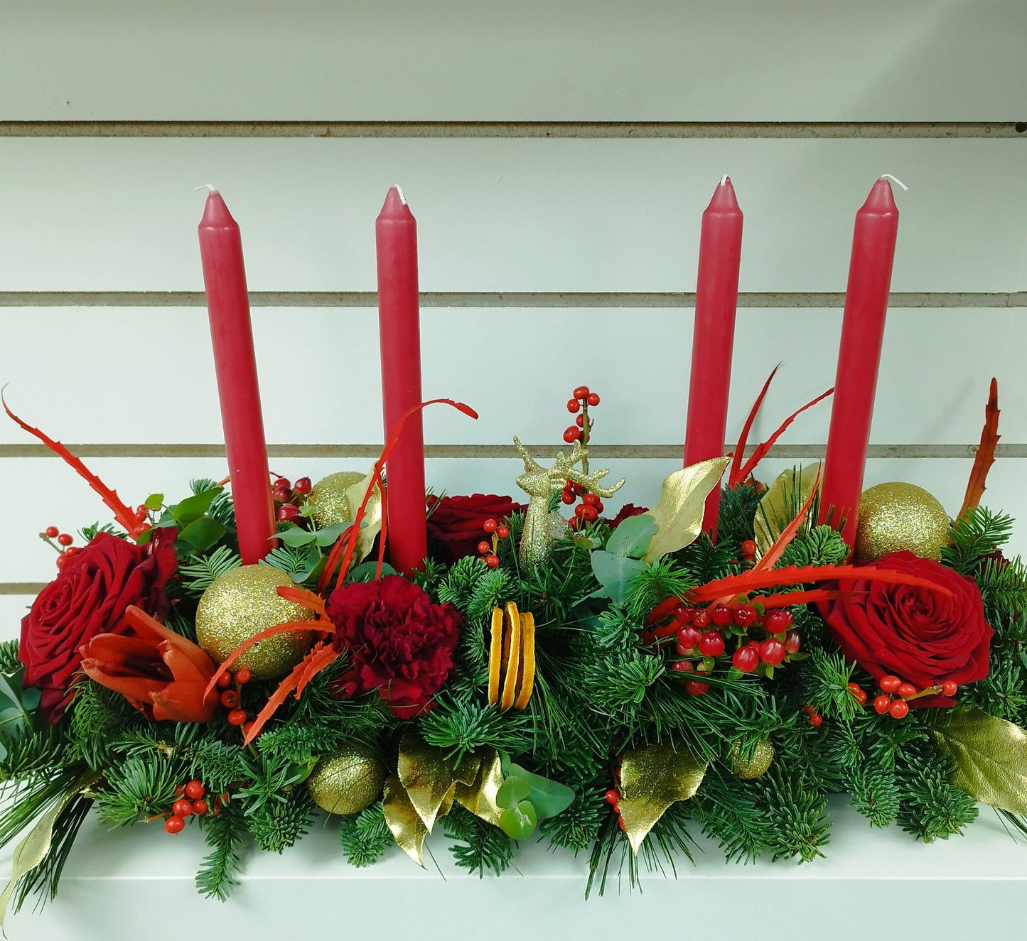 Decorative table centerpiece with red candles, greenery, and flowers on a nobble fir base.