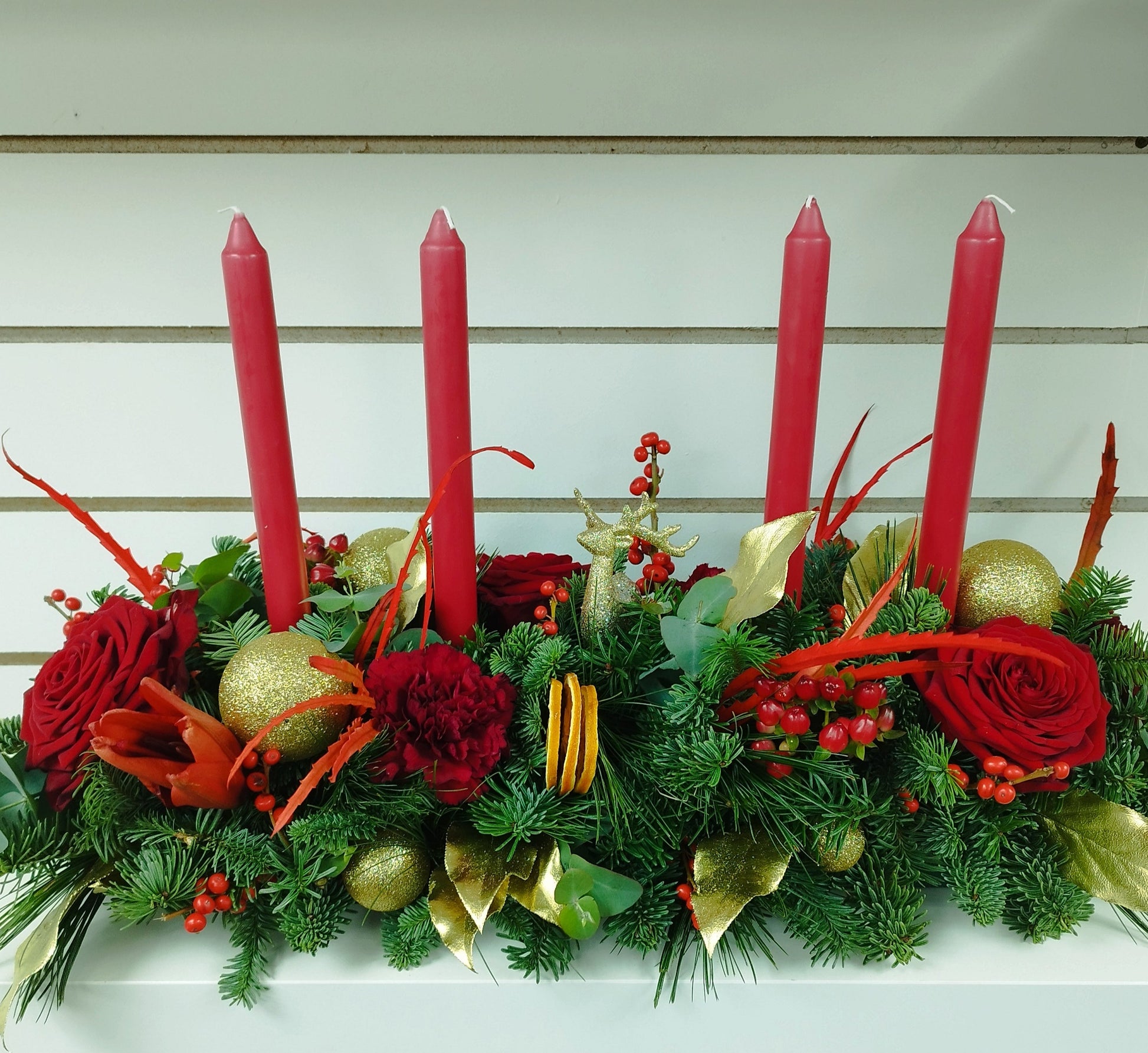 Decorative table centerpiece with red candles, greenery, and flowers on a nobble fir base.